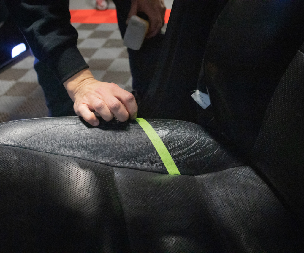 Image removing tape from BMW seat showing the difference after the leather has been cleaned.